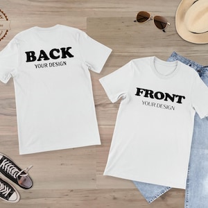 May include: Two white t-shirts with black text reading "BACK YOUR DESIGN" and "FRONT YOUR DESIGN". The shirts are on a wooden surface, alongside sunglasses, a straw hat, and a pair of blue jeans.