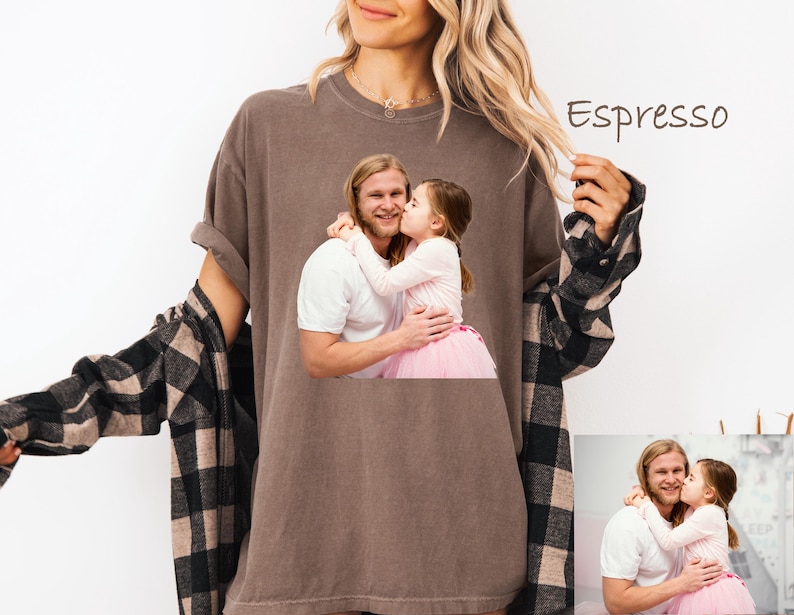May include: Espresso-colored t-shirt featuring a printed image of a man and a young girl embracing. The woman in the image is wearing the t-shirt and a black and brown plaid shirt. The text "Espresso" is written on the top right of the image.