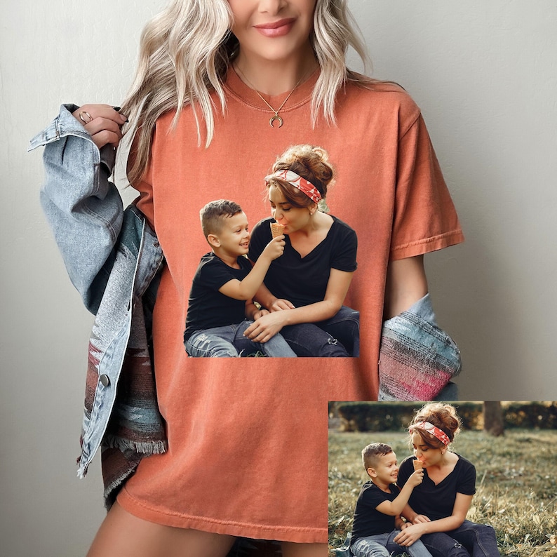 May include: Orange-red t-shirt featuring a printed image of a mother and child sharing an ice cream cone. The child is offering the ice cream to the mother. The shirt is a comfortable, casual style, suitable for everyday wear.