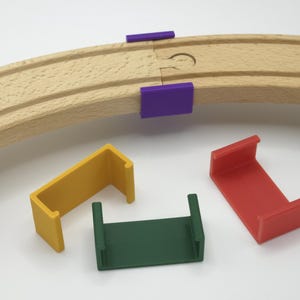 May include: Wooden toy train track with purple, yellow, green, and red track connectors. The track is curved and has a slot for the connectors. The connectors are U-shaped.