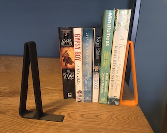 May include: A selection of books held by two bookends. The books have colourful covers and titles including "Gypsy Boy" and "A Thousand Splendid Suns." One bookend is black, the other is orange.