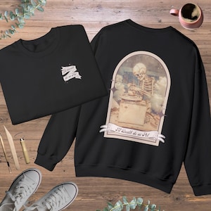 Peut inclure: Sweat-shirt noir avec un graphique d'un squelette travaillant sur un tour de potier. Le graphique est encadré d'une arche brun clair avec des étoiles et le texte "'Til Death do us 'Pot'" dans une bannière en dessous.
