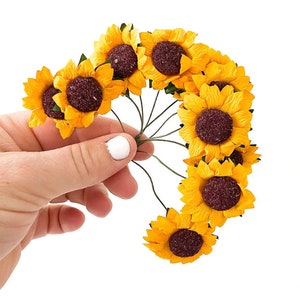 May include: A bunch of small, yellow paper sunflowers with brown centers. The sunflowers are attached to green wire stems.