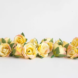 May include: A cluster of small, artificial roses in shades of yellow and peach. The roses have green leaves and are arranged in a single layer.