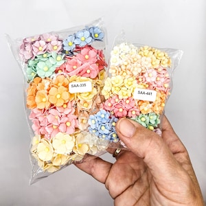 Op de afbeelding: Twee zakjes met pastelkleurige papieren bloemen. Het grotere zakje is gelabeld "SAA-335" en het kleinere zakje is gelabeld "SAA-441".