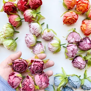 May include: Assortment of artificial flower buds in various colors, including pink, purple, blue, orange, and red. The flower buds are arranged on a white surface.