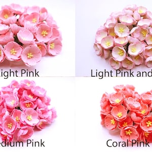 May include: A collection of paper flowers in various shades of pink and coral. The image displays four different color options: light pink, light pink and white, medium pink, and coral pink. Each flower has a yellow center.