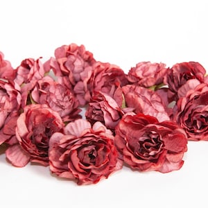 May include: A cluster of burgundy-colored artificial rose buds, arranged in a loose pile on a white background.