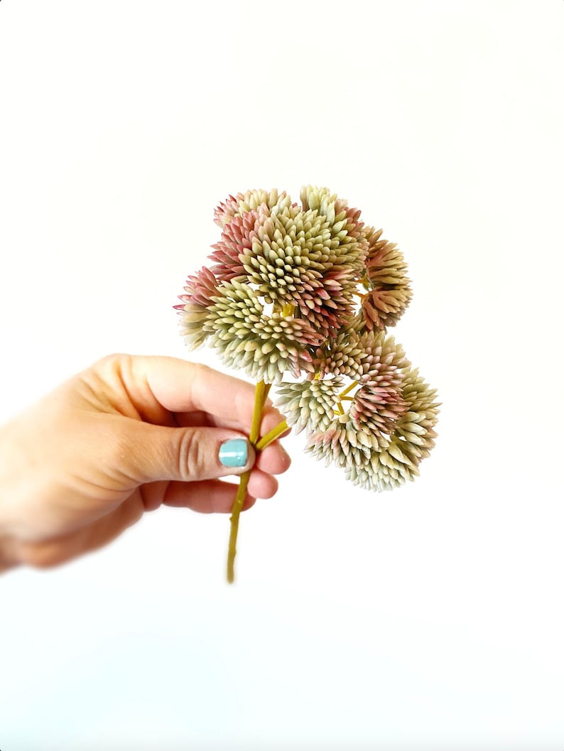 以下が含まれることがあります： 緑とピンクのグラデーションでできた、人工の花の頭が3つあるブーケ。花は小さな尖った花びらでできており、1本の茎につけられています。