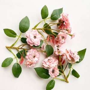 May include: A cluster of pink artificial roses with green leaves arranged on a white background.