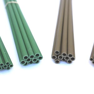 May include: Four bundles of thin, cylindrical rods arranged in a row. Two bundles are forest green and two are brown. Each rod features a fine, ribbed texture along its length and a hollow, circular opening at the end, secured by a tan rubber band.