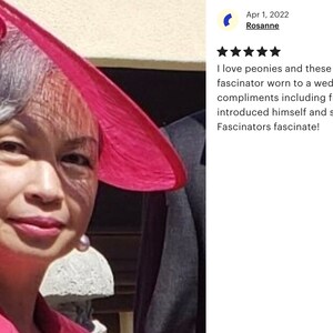 Peut inclure: Une femme portant un chapeau rose avec une grande fleur rose sur le dessus. Le chapeau est inclin&eacute; et la femme regarde la cam&eacute;ra. La femme porte une veste rose et a les cheveux gris. Le texte "Fascinators fascinate!" est visible sur l'image.