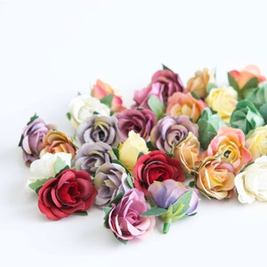 May include: A collection of small, artificial roses in various shades of pink, purple, red, yellow, and white. The roses are arranged in a loose cluster on a white background.