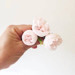 May include: Three pale pink artificial flowers with green stems. The flowers are arranged in a cluster and are held in a hand.