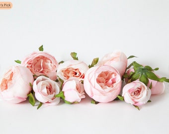 May include: A cluster of pale pink artificial roses with green leaves. The roses are arranged in a row on a white background.