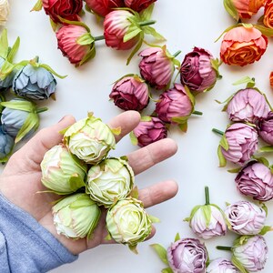May include: A collection of artificial flower buds in various colors, including pink, red, orange, green, and blue. The buds are arranged in a hand, with the green buds in the center.