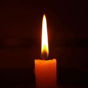 Puede incluir: Una sola vela con una llama naranja brillante ardiendo en una habitación oscura.