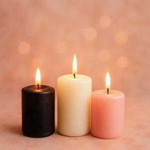 May include: Three candles, one black, one white and one pink, are lit and arranged in a row on a pink background.