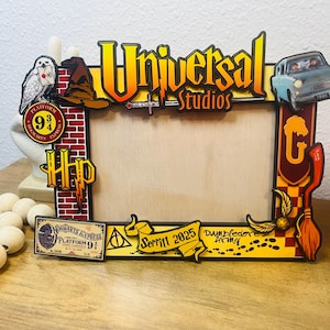 May include: Wooden photo frame with a Universal Studios and Harry Potter theme. Features a light blue car, a Hogwarts Express ticket, and the words "Universal Studios" in yellow and orange. Includes a brick wall design and a broom.