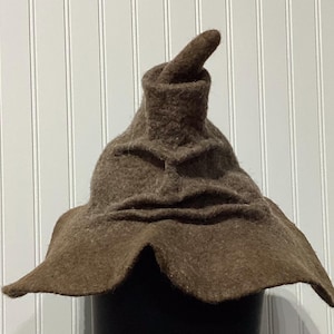 May include: A brown, felt Sorting Hat with a pointed top and wide brim. The hat has a textured appearance and is slightly crumpled, with a prominent fold near the base of the point. The hat is a prop from the Harry Potter series.