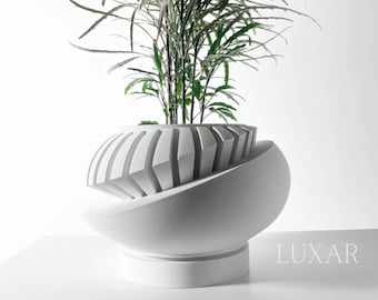 May include: White ceramic planter with a geometric design. The planter has a wide, rounded base and a narrow opening at the top. A green plant is growing out of the planter.