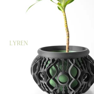May include: A black decorative plant pot with a unique openwork design, holding a green plant. The pot has a rounded shape and a contrasting green interior. The word "LYREN" is printed in green.