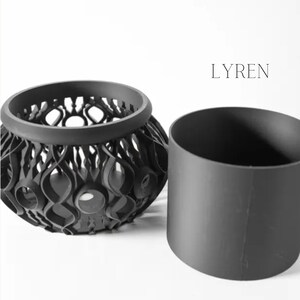 May include: A black decorative bowl with an openwork design and a separate cylindrical insert. The bowl has a rounded shape with intricate, swirling patterns. The word "LYREN" is printed in the upper right corner.