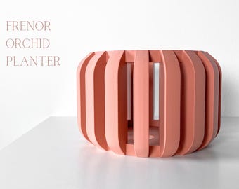 May include: A coral-colored, cylindrical planter with vertical slats. The planter has a modern design and is labeled "Frenor Orchid Planter" in the upper left corner. The planter is on a white surface.