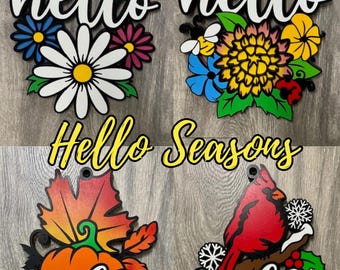 May include: Four wooden signs with the word "hello" in white lettering and different seasonal designs. The first sign features a butterfly and flowers, the second a sun, the third a pumpkin and sunflower, and the fourth a cardinal and snowflakes. The signs are all part of a set called "Hello Seasons".
