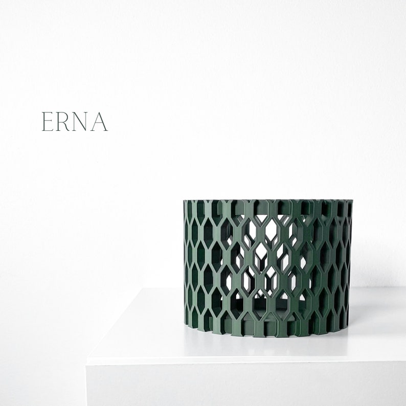 May include: A dark green cylindrical decorative object with a geometric honeycomb pattern. The object is displayed on a white surface against a white background. The word "ERNA" is printed in a minimalist font.