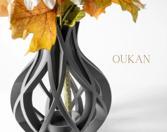 May include: A dark gray decorative vase with a unique openwork design, holding colorful autumn leaves. The vase has a cylindrical interior and a decorative exterior with the word "OUKAN" in brown.
