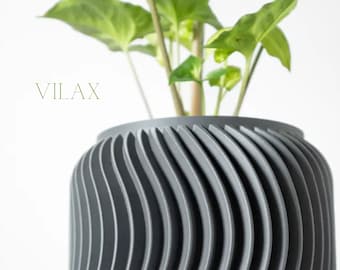 May include: A gray, ribbed planter pot with a spiral design, holding a green leafy plant. The word "VILAX" is printed in green on the left side. The pot has a modern, minimalist aesthetic.