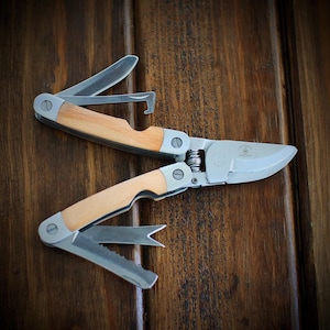 May include: A multi-tool gardening shears with wooden handles. The shears have a pruning blade, a wire cutter, and a bottle opener.