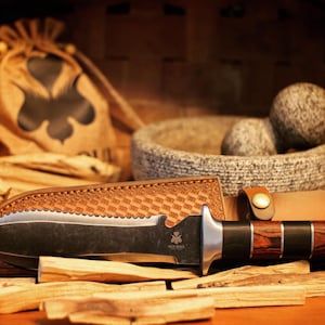 May include: A black and silver knife with a wooden handle, resting on a pile of wooden sticks. The knife has a serrated blade and a leather sheath. The knife is surrounded by other items, including a small bag and a bowl.