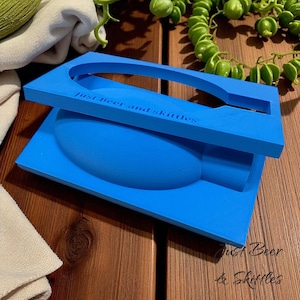 May include: A vibrant blue beer and Skittles holder. The text "Just Beer and Skittles" is printed on the top and bottom. The holder is designed to hold a beer bottle and a bag of Skittles. It is made of a solid material.