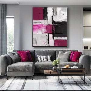 May include: Abstract art print featuring pink, black and white geometric shapes. The print is framed and hanging on a grey wall above a grey sectional sofa.