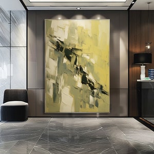 May include: Large abstract painting in a gold frame. The artwork uses yellow, green, black, and white brushstrokes, forming a textured, geometric design. The painting is displayed in a modern interior with a dark grey chair and marble flooring.