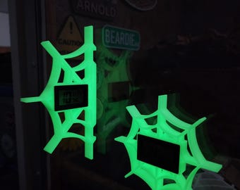 Op de afbeelding: Twee gloeiende groene spinnenwebvormige digitale klokken. De klokken tonen de tijd en zijn gemonteerd op een donkere ondergrond. Het spinnenwebontwerp is gedetailleerd, met een heldere, neon-groene kleur.