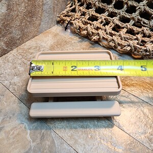 May include: A miniature beige picnic table, measuring 7.6 cm wide, as shown by a tape measure. The table is made of plastic and has a simple design.