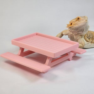 May include: A pink plastic picnic table with two benches. The table is small and would be suitable for a small pet or reptile.