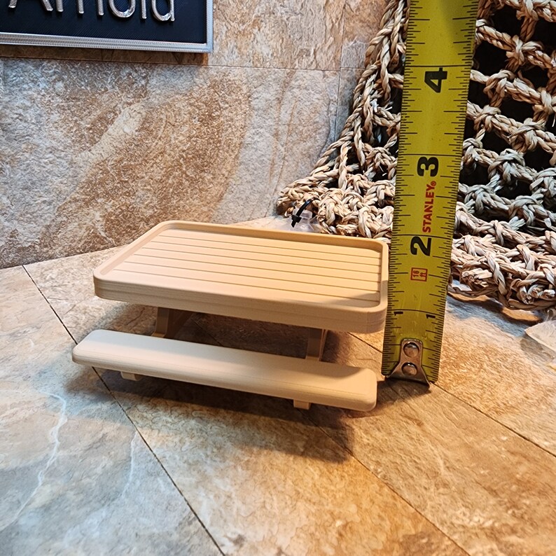 May include: A miniature wooden picnic table with a light brown finish. The table is approximately 18 cm long and 10 cm wide. The table has a bench on one side.