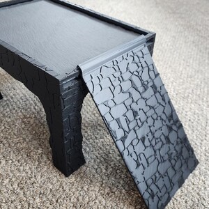 Może przedstawiać: Czarny drewniany st&oacute;ł z fakturowaną powierzchnią i czarna rampa z fakturowaną powierzchnią. St&oacute;ł i rampa są połączone.