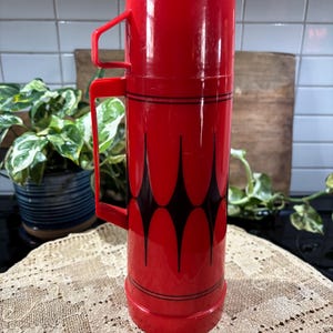 May include: Red thermos with a black geometric design. The thermos has a handle and a lid.