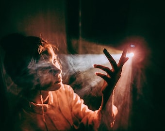 Puede incluir: Perfil de una persona iluminado por una luz brillante, con la mano extendida hacia ella. La imagen tiene una atmósfera oscura y se centra en el rostro y la mano de la persona, con un efecto de humo.