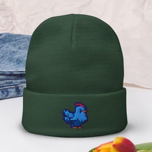 May include: A dark green beanie with a blue pixelated chicken embroidered on the front.