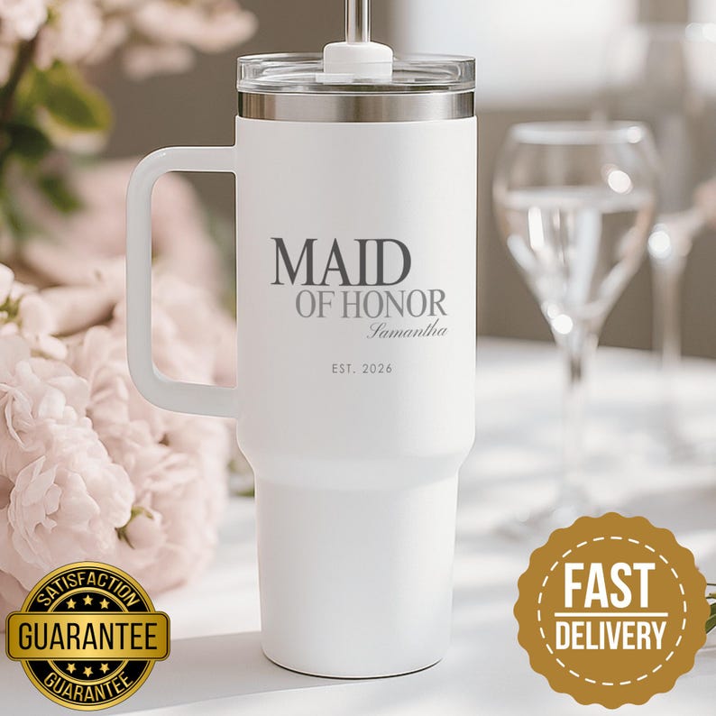 May include: A white stainless steel tumbler with a handle and a clear lid featuring a straw. The front is printed with the dark grey text MAID OF HONOR, the name Samantha in script, and the date EST. 2026 centered on the cylindrical body.