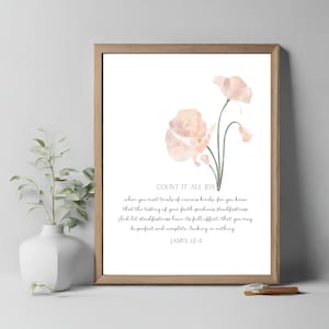 May include: A framed print featuring a watercolor floral design in soft peach tones. The artwork includes the text "COUNT IT ALL JOY" and a Bible verse from James 12-4. The frame is a light brown color.