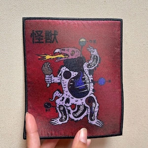 May include: A red embroidered patch with a black border featuring a cartoon creature with a bird head, a purple body, and a chicken leg in its hand. The creature has a blue flame inside its body and the text "怪獣" in black on the top left corner.