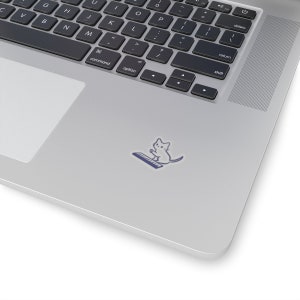 Pode incluir: Um autocolante branco com um gato de desenho animado a tocar um teclado de piano azul. O autocolante está colocado numa superfície prateada de um portátil, com o teclado visível no fundo.