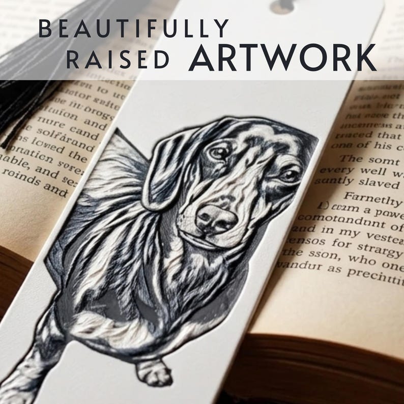 May include: A white bookmark featuring a black and white raised illustration of a dachshund dog. The bookmark includes a black tassel at the top and the text BEAUTIFULLY RAISED ARTWORK printed in black across the upper portion of the bookmark.
